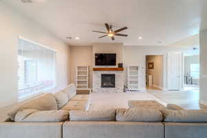 Living room with ceiling fan, a stone fireplace, and light wood-type flooring