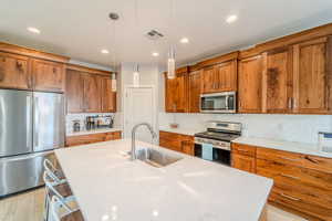 Kitchen featuring appliances with stainless steel finishes, pendant lighting, light wood-type flooring, a kitchen island with sink, and sink