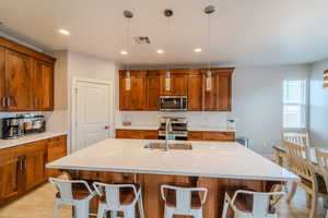 Kitchen featuring a kitchen bar, appliances with stainless steel finishes, hanging light fixtures, and sink