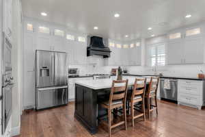 Kitchen featuring dark hardwood / wood-style floors, white cabinetry, a kitchen island, custom range hood, and stainless steel appliances