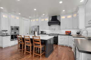 Kitchen with a center island, appliances with stainless steel finishes, white cabinetry, and premium range hood