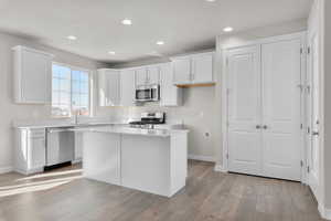 Kitchen with white cabinets, appliances with stainless steel finishes, sink, light hardwood / wood-style floors, and a center island