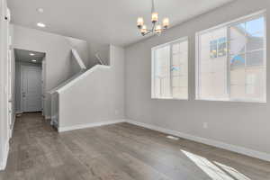 Empty room featuring an inviting chandelier, hardwood / wood-style flooring, and a wealth of natural light