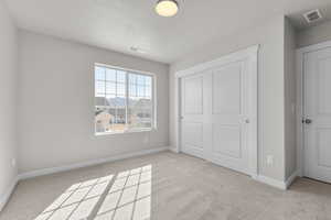 Unfurnished bedroom with a closet, a textured ceiling, and light colored carpet