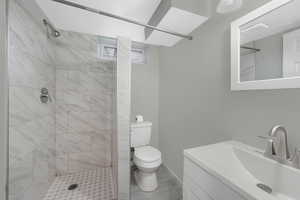 Bathroom featuring a tile shower, vanity, and toilet