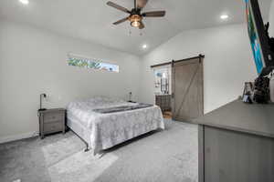 Bedroom with vaulted ceiling, a barn door, ceiling fan, ensuite bath, and light carpet