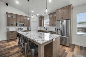 Kitchen with dark hardwood / wood-style floors, tasteful backsplash, a kitchen island, appliances with stainless steel finishes, and decorative light fixtures