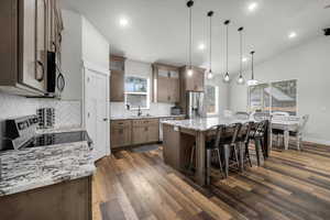 Kitchen with light stone counters, stainless steel appliances, a center island, vaulted ceiling, and dark hardwood / wood-style flooring