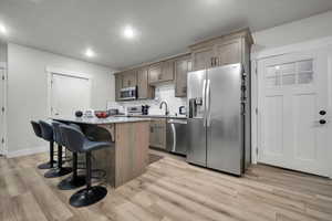 ADU Kitchen featuring light stone counters, light hardwood / wood-style flooring, appliances with stainless steel finishes, a center island, and a breakfast bar area