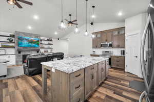 Kitchen with ceiling fan, light stone counters, lofted ceiling, appliances with stainless steel finishes, and a fireplace