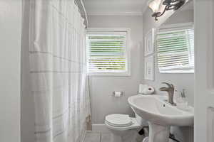 Bathroom with ornamental molding, toilet, tile patterned floors, and a shower with curtain