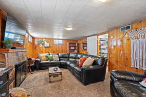 Carpeted living room with wooden walls and a stone fireplace