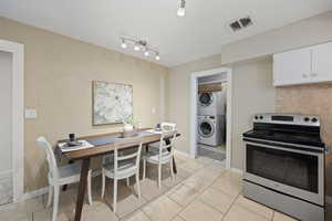 Kitchen with stacked washer and dryer, light tile patterned flooring, white cabinets, electric stove, and rail lighting