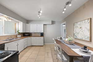 Kitchen with white cabinets, light tile patterned floors, sink, backsplash, and black appliances