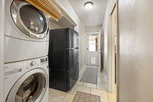 Clothes washing area featuring stacked washer / drying machine and light tile patterned floors