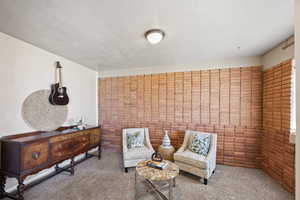 Living area featuring carpet, a textured ceiling, and brick wall