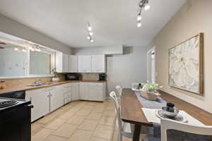 Kitchen with sink, white cabinets, rail lighting, black appliances, and backsplash