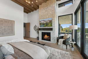 Bedroom with high vaulted ceiling, beamed ceiling, wooden ceiling, a fireplace, and light hardwood / wood-style floors