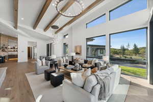 Living room with lofted ceiling with beams, light hardwood / wood-style flooring, and a notable chandelier