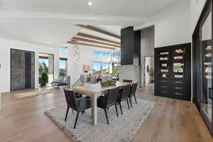 Dining space featuring beam ceiling, light wood-type flooring, a fireplace, and a high ceiling