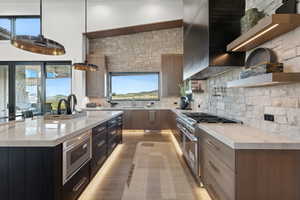 Kitchen featuring decorative backsplash, wall chimney range hood, decorative light fixtures, stainless steel stove, and an island with sink