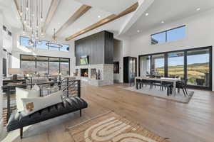 Living room featuring beam ceiling, a fireplace, a high ceiling, and light wood-type flooring