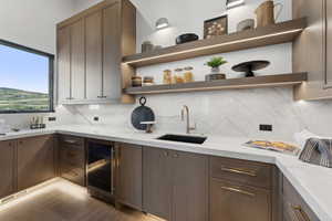 Kitchen with light stone countertops, backsplash, beverage cooler, and sink