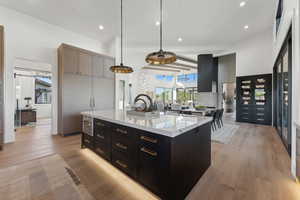 Kitchen with light stone countertops, pendant lighting, beamed ceiling, light hardwood / wood-style floors, and an island with sink