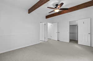 Primary bedroom with ceiling fan, beamed ceiling, and light carpet