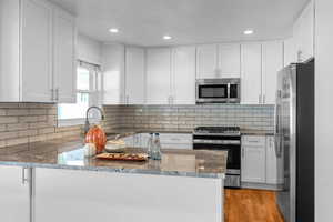 Kitchen featuring light stone counters, sink, kitchen peninsula, white cabinetry, and stainless steel appliances