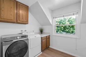 Upstairs laundry room featuring light wood-type flooring, independent washer and dryer, and cabinets