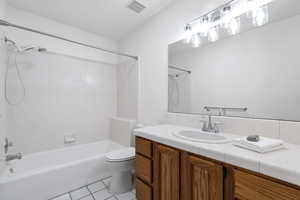 Primary bathroom featuring tile patterned flooring, tiled shower / bath, vanity, and toilet