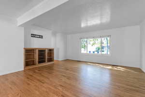 Unfurnished living room with hardwood / wood-style flooring, crown molding, and a textured ceiling