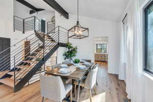 Dining room with a chandelier, light LVP flooring, lofted ceiling with beams, and a wealth of natural light opens on to the kitchen.