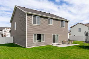 Back of property featuring a patio, a yard, and a trampoline