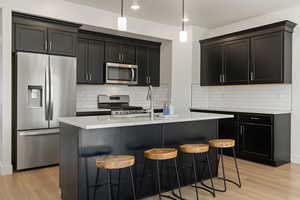 Kitchen featuring a kitchen island with sink, appliances with stainless steel finishes, backsplash, and light hardwood / wood-style flooring