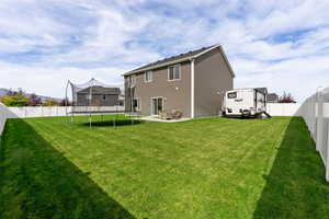 Back of property with a lawn, a patio, and a trampoline