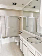 Full bathroom with bath / shower combo with glass door, vanity, tile patterned flooring, ornamental molding, and toilet