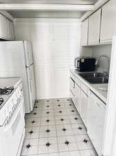 Kitchen with white cabinets, light tile patterned flooring, sink, and white appliances