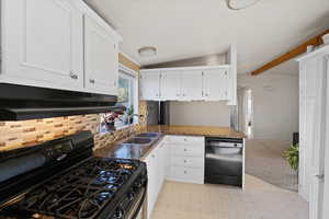 Kitchen featuring dark stone counters, sink, beam ceiling, white cabinetry, and black appliances