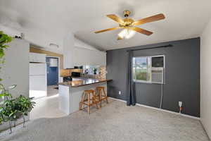 Kitchen with vaulted ceiling, tasteful backsplash, white cabinets, kitchen peninsula, and ceiling fan