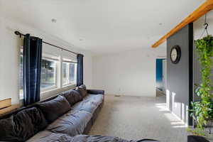 Carpeted living room featuring vaulted ceiling with beams