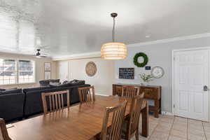 Tiled dining space featuring ornamental molding, ceiling fan, and a textured ceiling