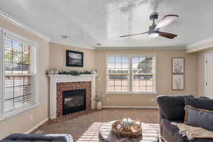 Living room featuring crown molding, ceiling fan, light colored carpet, and a brick fireplace