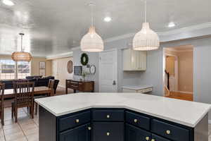 Kitchen featuring ornamental molding, light tile patterned floors, a kitchen island, and blue cabinetry