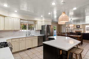 Kitchen featuring appliances with stainless steel finishes, hanging light fixtures, a tiled fireplace, light tile patterned floors, and sink