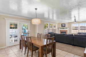 Tiled dining area with a textured ceiling, crown molding, ceiling fan, and a brick fireplace