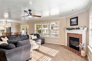 Carpeted living room with a textured ceiling, crown molding, ceiling fan, and a brick fireplace