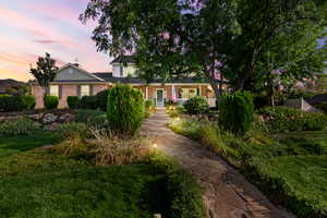 Twilight view of front facade with a porch and a yard