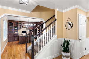 Stairs featuring a notable chandelier, wood-type flooring, a textured ceiling, and crown molding